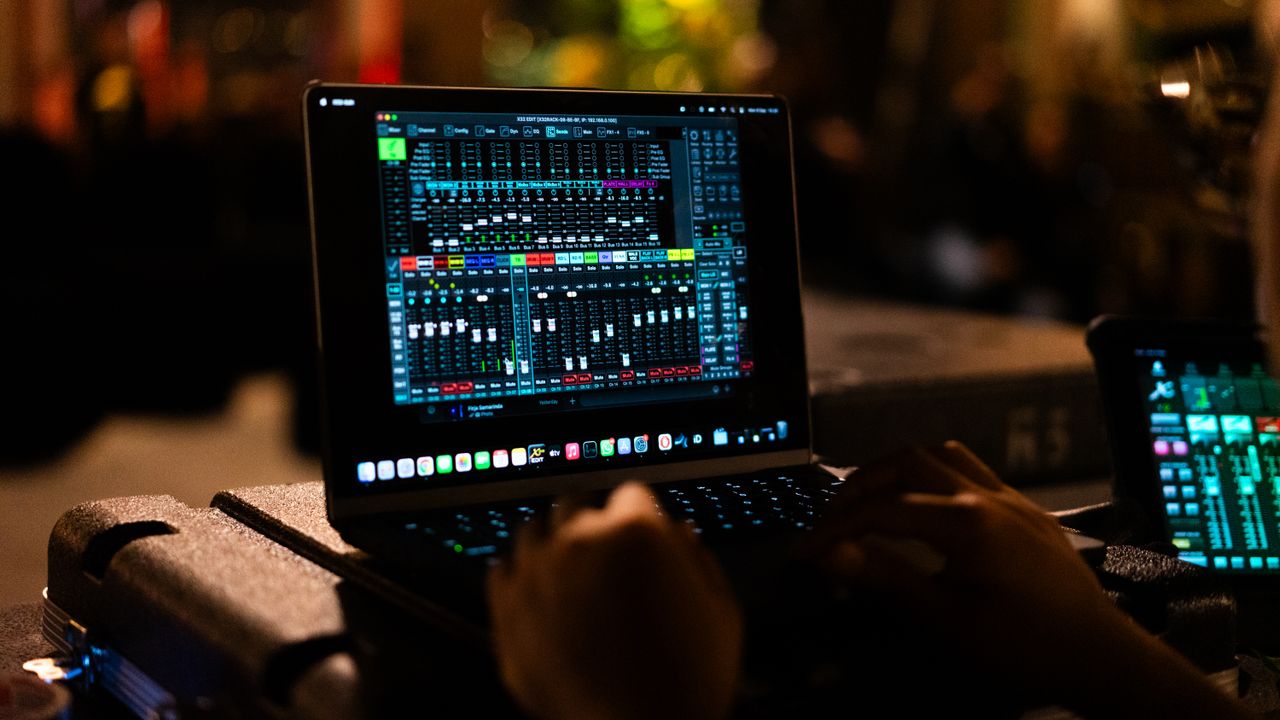 A professional using a digital audio mixer on a laptop in a recording studio setting.